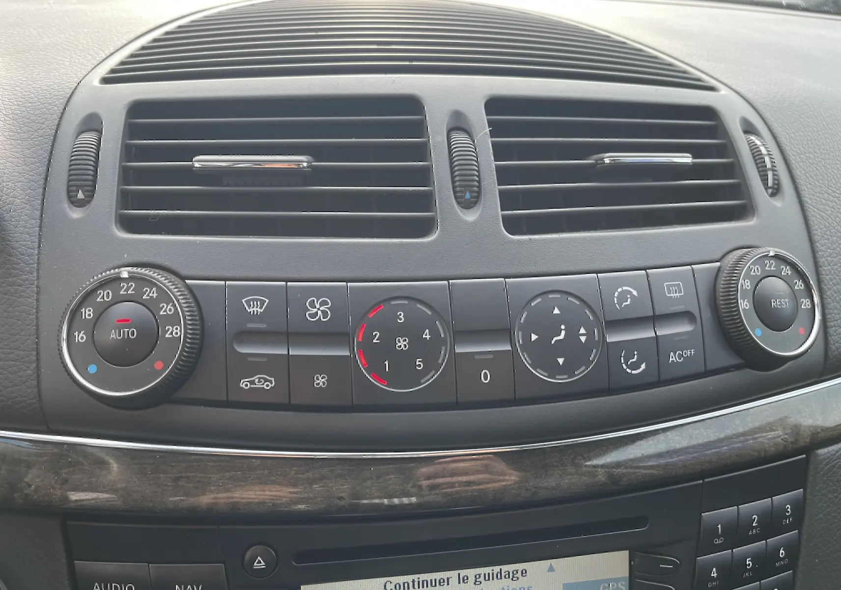 Gros plan sur la console centrale noire de la Mercedes Classe E 320 CDI 2003, montrant les commandes de climatisation et ventilation.