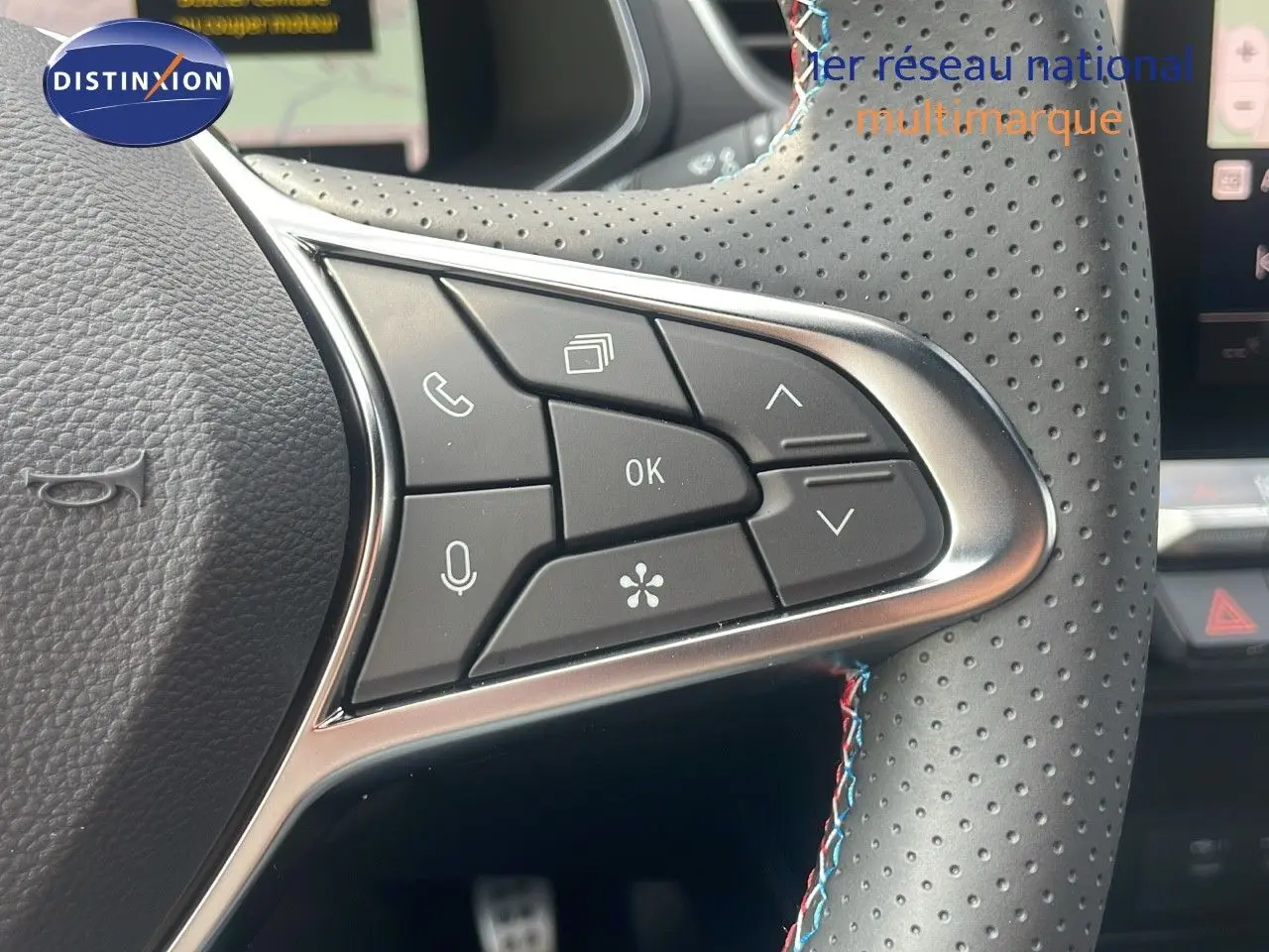 Gros plan sur les commandes gauche du volant perforé du Renault Captur gris Cassiopée avec surpiqûres tricolores.