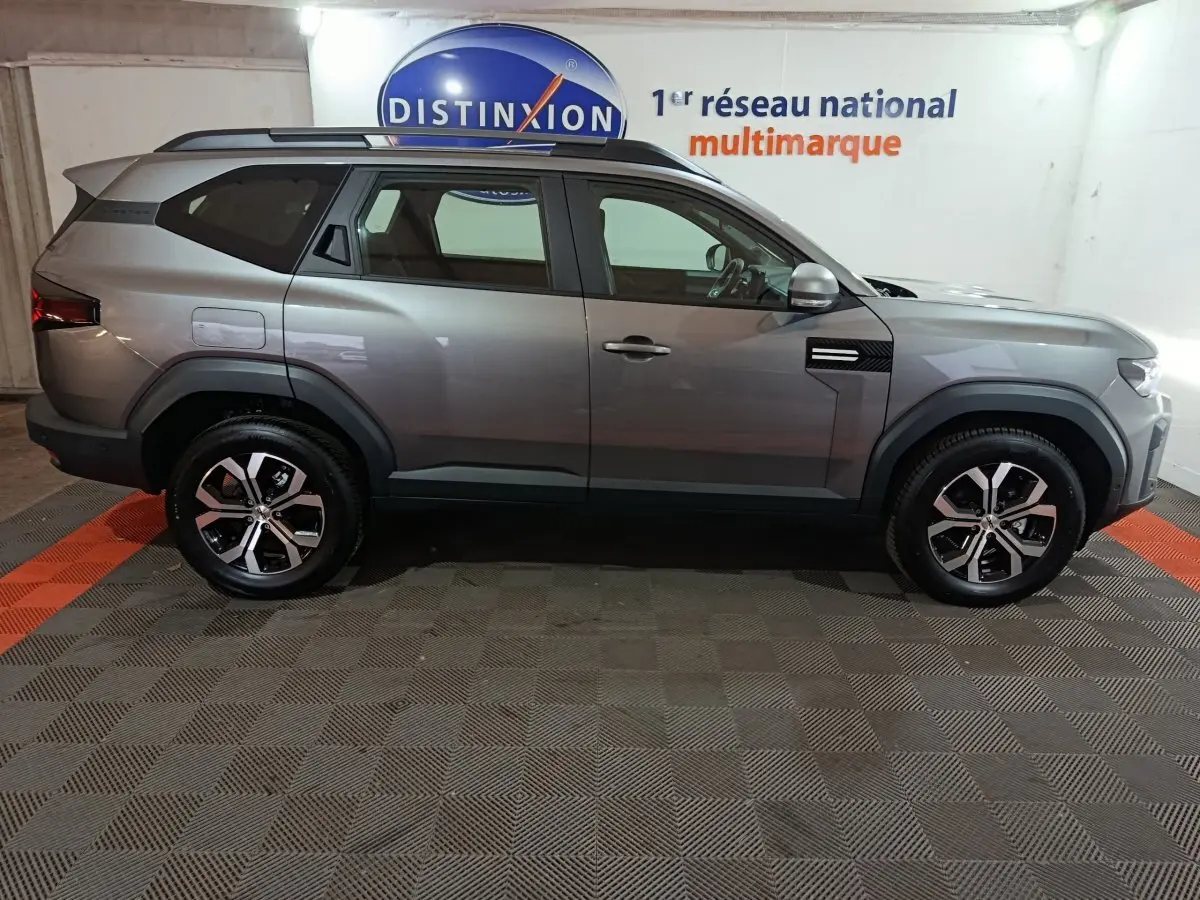 Vue de profil côté droit du SUV Dacia Bigster gris foncé avec jantes alliage et barres de toit noires.