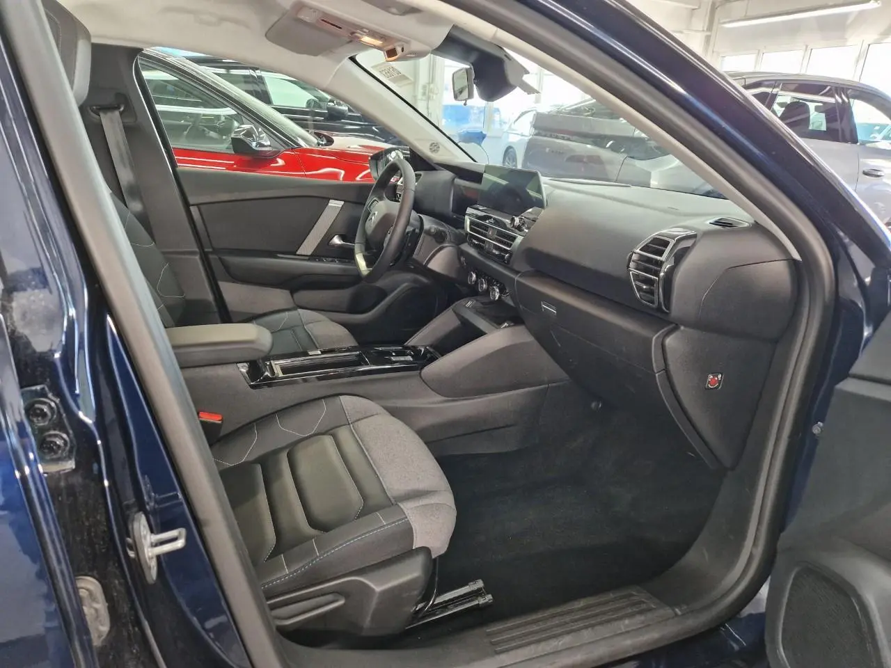 Intérieur avant droit d'une Citroën C4 2024 bleu Eclipse, avec sièges bicolores gris et noir et tableau de bord moderne.