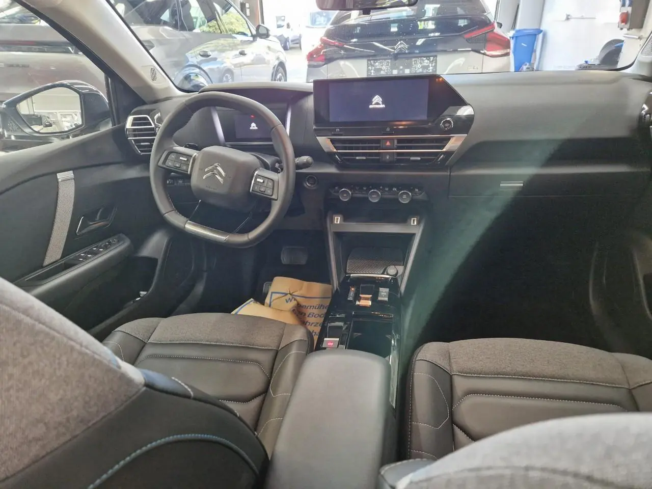 Vue intérieure avant de la Citroën C4 2024, avec tableau de bord noir et sièges en tissu gris et noir.