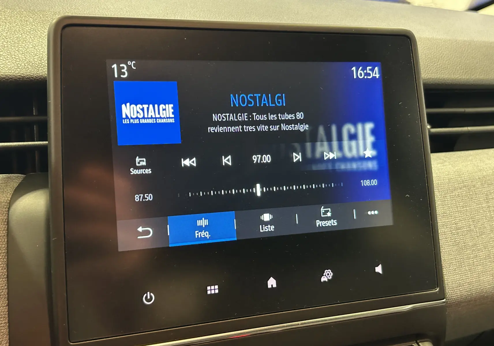 Écran tactile central de la Renault Clio V blanc affichant la radio Nostalgie à 97 FM, température 13°C, vue intérieure.