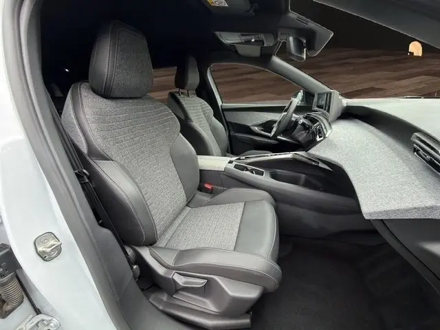 Vue intérieure côté conducteur du Peugeot 5008 blanc 2025, sièges tissu et cuir, tableau de bord moderne avec écran tactile.