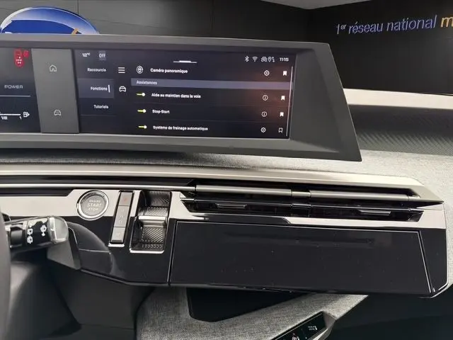 Vue rapprochée du tableau de bord noir du Peugeot 5008 blanc 2025, avec écran tactile multifonctions allumé.