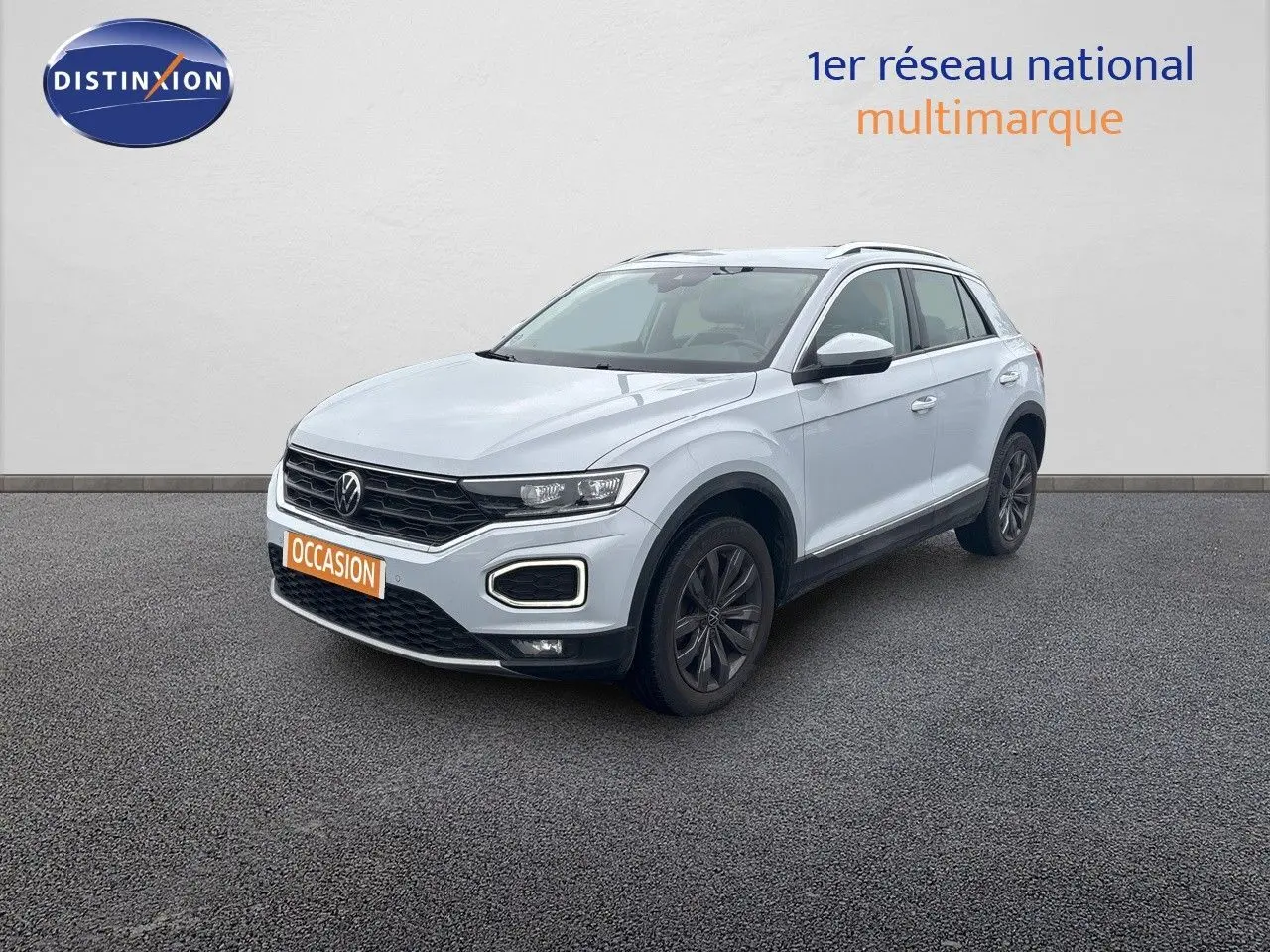 Volkswagen T-Roc blanc argenté en 3/4 avant droit, avec calandre noire et jantes foncées sur sol gris.