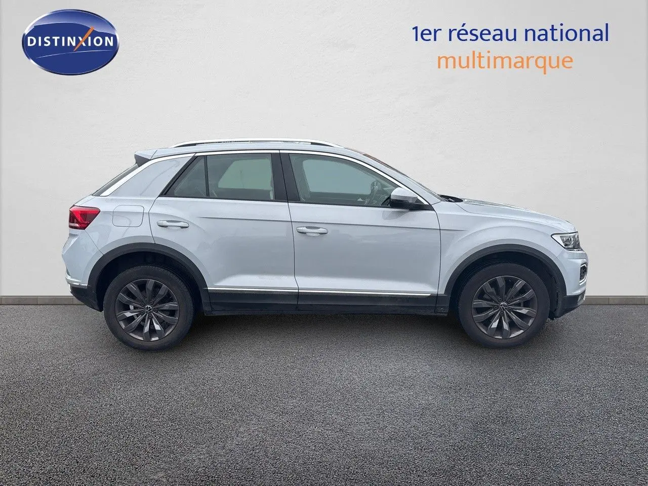 Profil côté gauche d'un Volkswagen T-Roc blanc argenté 2021 avec jantes foncées sur fond neutre.