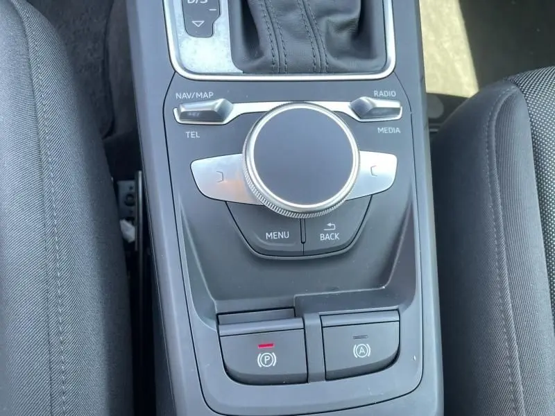 Vue rapprochée de la console centrale noire de l'Audi Q2 TFSI 150CV avec commandes multimédia et frein à main électrique.