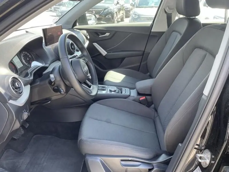 Intérieur côté conducteur de l'Audi Q2 TFSI 150CV noir métal 2022, sièges tissu gris et tableau de bord moderne.