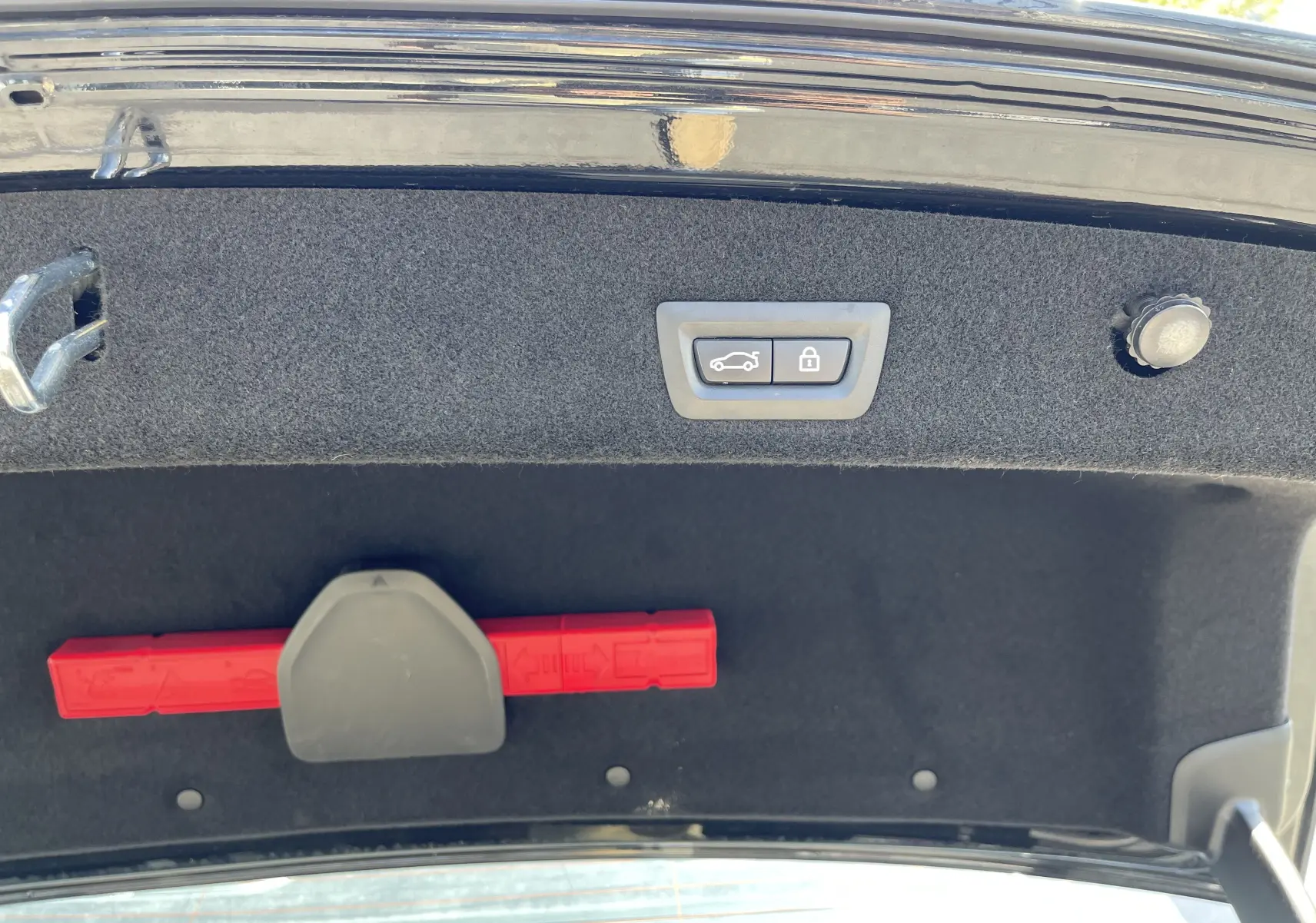 Intérieur du coffre de la BMW Série 7 noire, vue du hayon ouvert avec bouton de fermeture électrique et triangle de signalisation rouge.