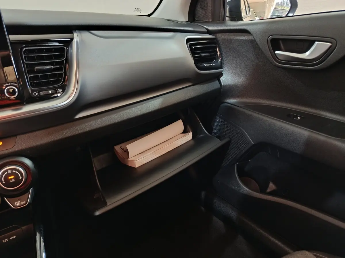 Intérieur côté passager du Kia Stonic gris clair 2022, avec boîte à gants ouverte contenant un manuel.