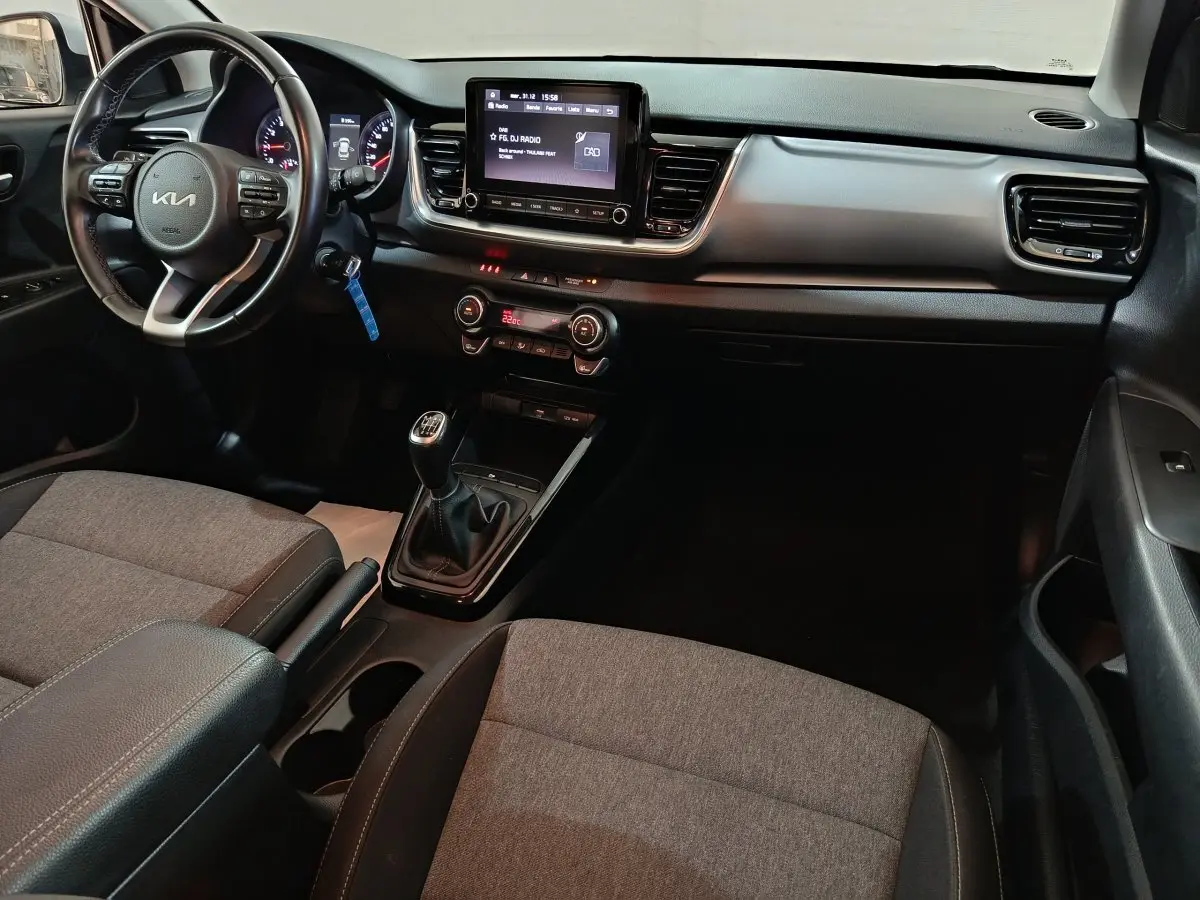 Vue intérieure côté conducteur du tableau de bord et console centrale du KIA Stonic gris clair avec boîte manuelle et écran tactile.