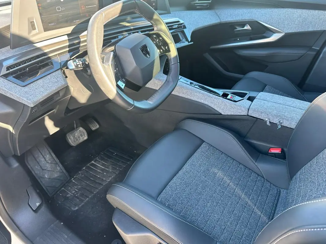 Intérieur avant droit du Peugeot 3008 Hybrid 145 Allure 2025, sièges tissu et cuir gris, tableau de bord moderne avec volant compact.