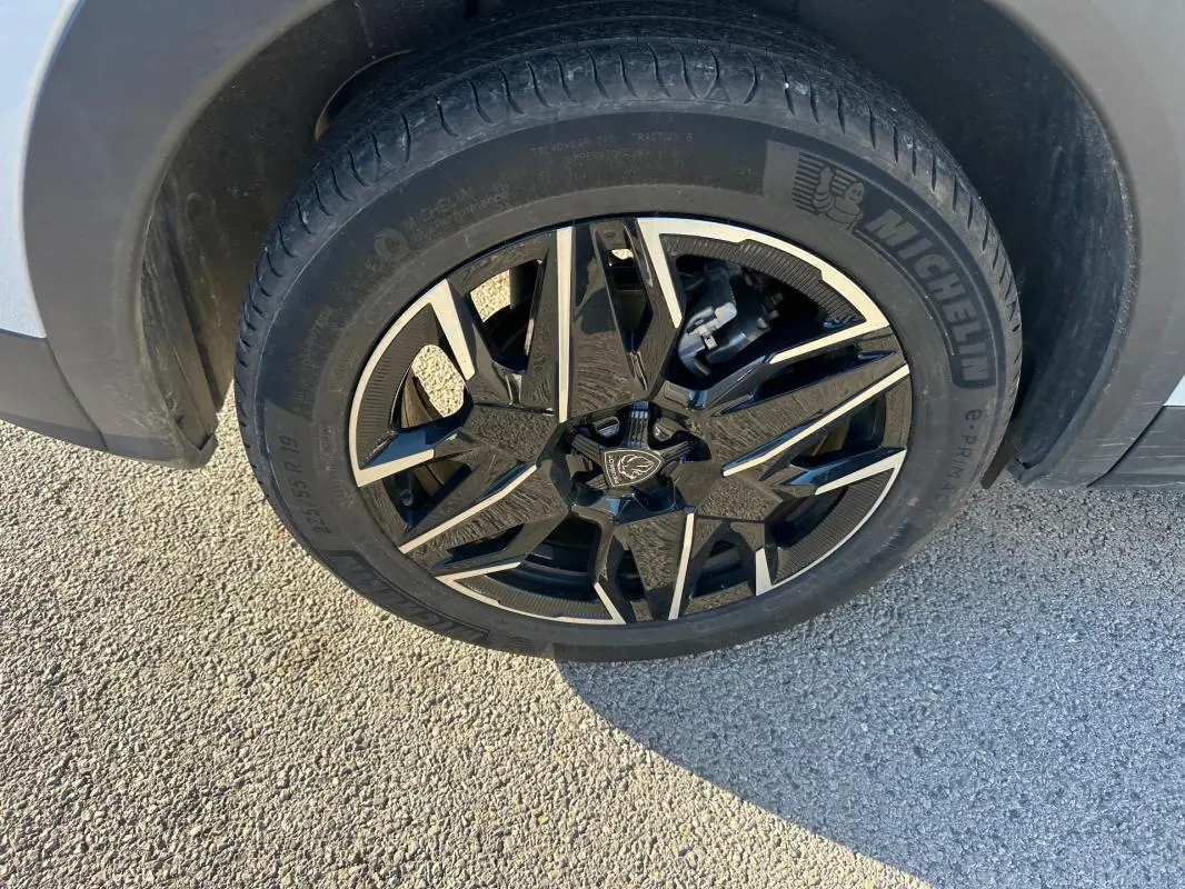 Gros plan sur la jante alliage 19 pouces noire et argentée du Peugeot 3008 Hybrid blanc, côté gauche arrière.