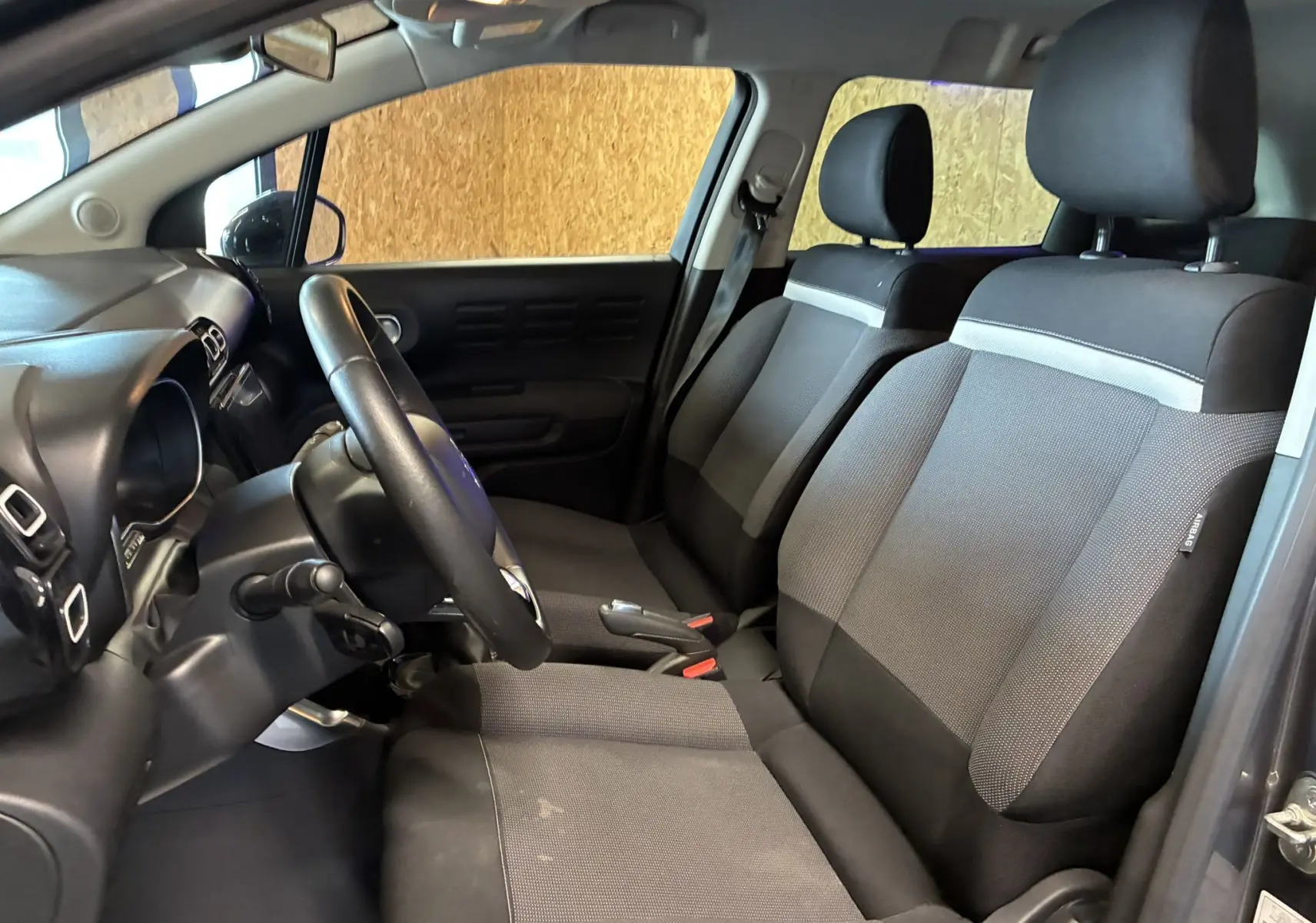Vue intérieure côté conducteur du Citroën C3 Aircross 2023 avec sièges tissu gris noir et volant cuir multifonction.