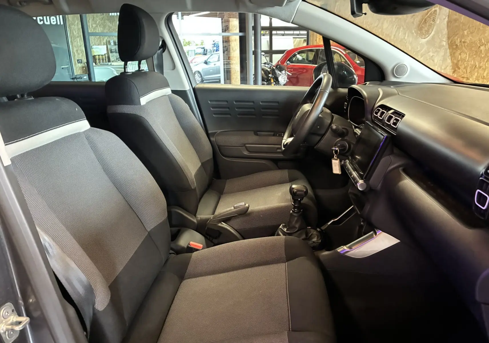 Intérieur côté conducteur du Citroën C3 Aircross 2023, sièges tissu gris noir et tableau de bord avec écran tactile.