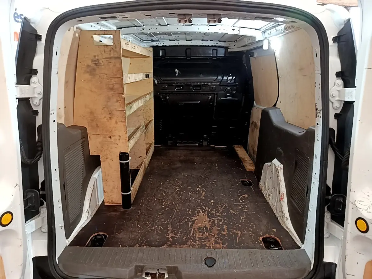Vue arrière du fourgon Ford Transit blanc 2022, montrant l’intérieur utilitaire avec étagères en bois à gauche.