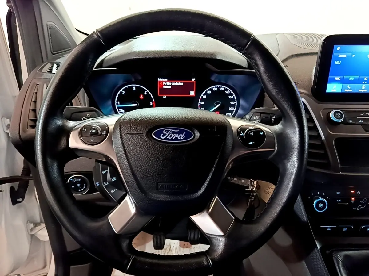 Vue intérieure centrée sur le volant noir Ford du Transit Fourgon blanc avec tableau de bord et écran tactile.