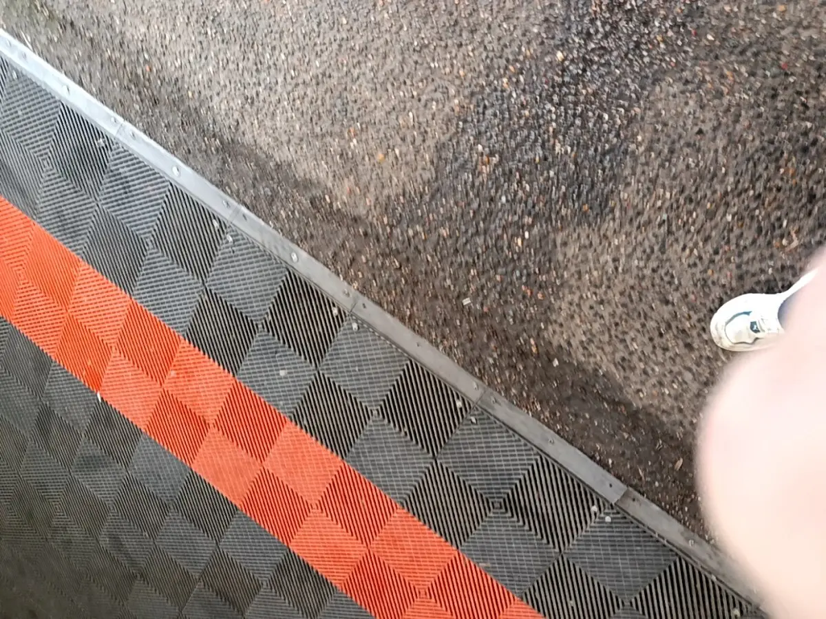 Vue partielle du sol avec un tapis en damier noir et rouge, sans véhicule visible.