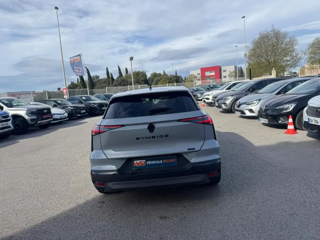 Vue arrière d'une Renault SYMBIOZ gris clair 2025 avec feux LED effilés et logo central noir sur parking.