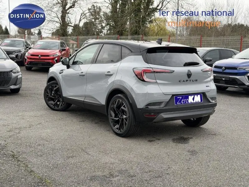 Renault Captur 1.8 E-Tech hybride 2026 en gris Rafale/noir, vue 3/4 arrière avec jantes noires et toit noir.