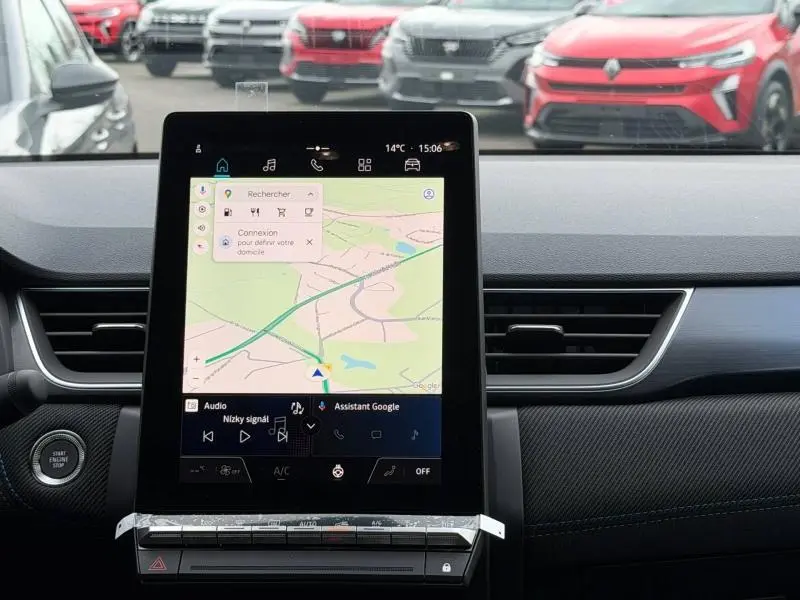 Vue intérieure centrée sur l'écran tactile du tableau de bord du Renault Captur 2026, avec vue floue sur des véhicules rouges à l'extérieur.