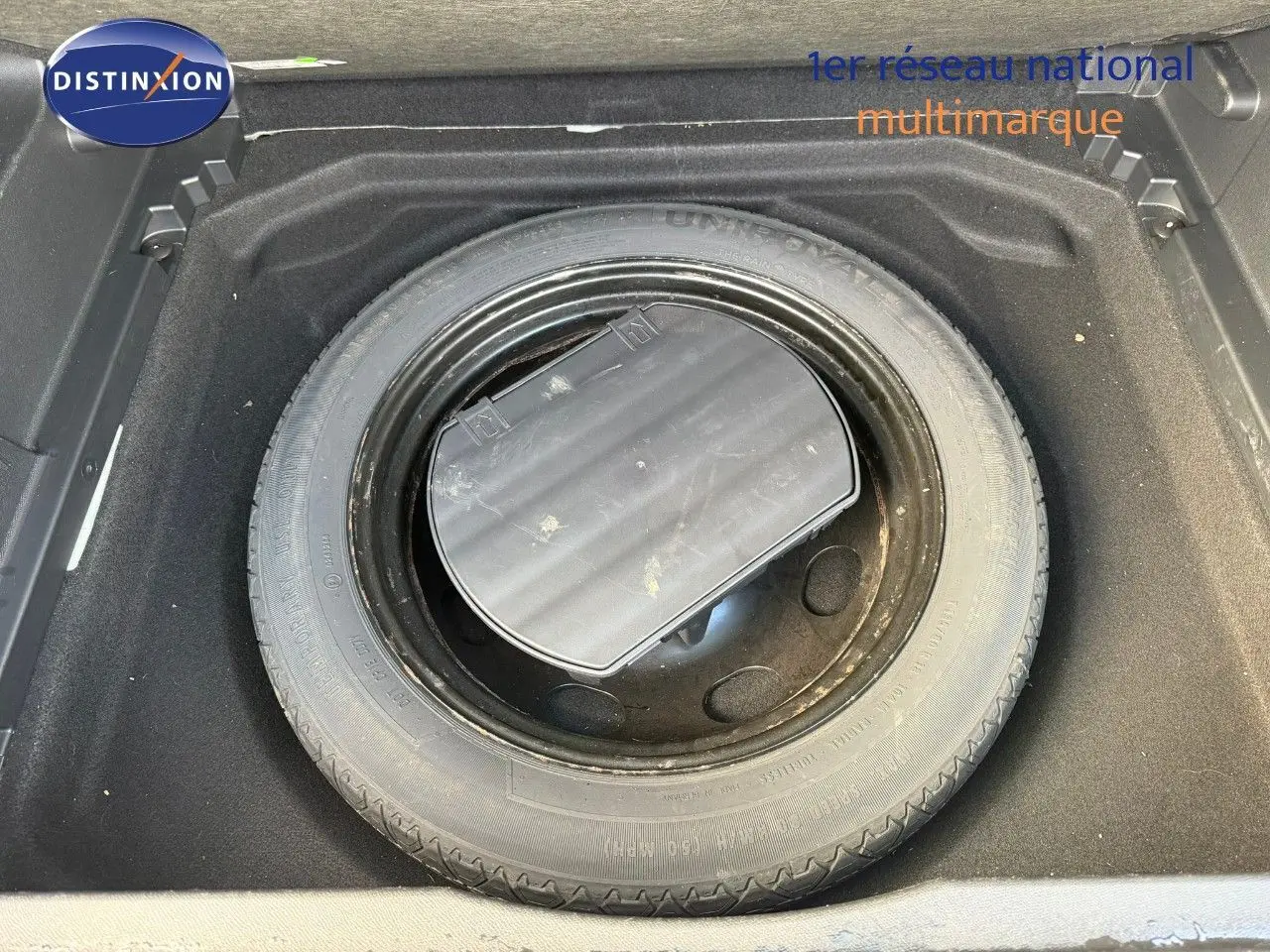 Pneu de secours noir logé dans le coffre d'un Citroën C5 Aircross blanc nacré, vue plongeante sur le rangement.