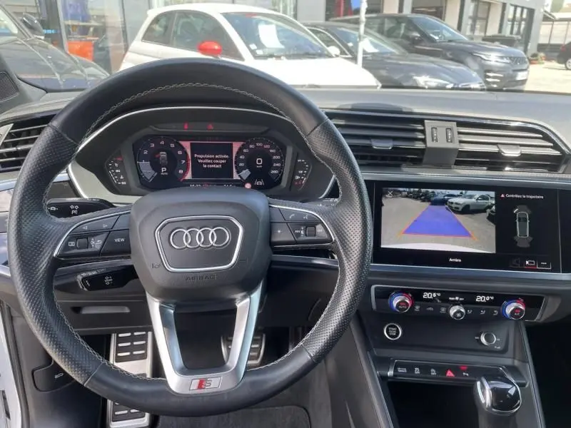 Vue intérieure centrée sur le volant S-Line et le tableau de bord numérique de l'Audi Q3 blanc 2021 avec écran de recul.