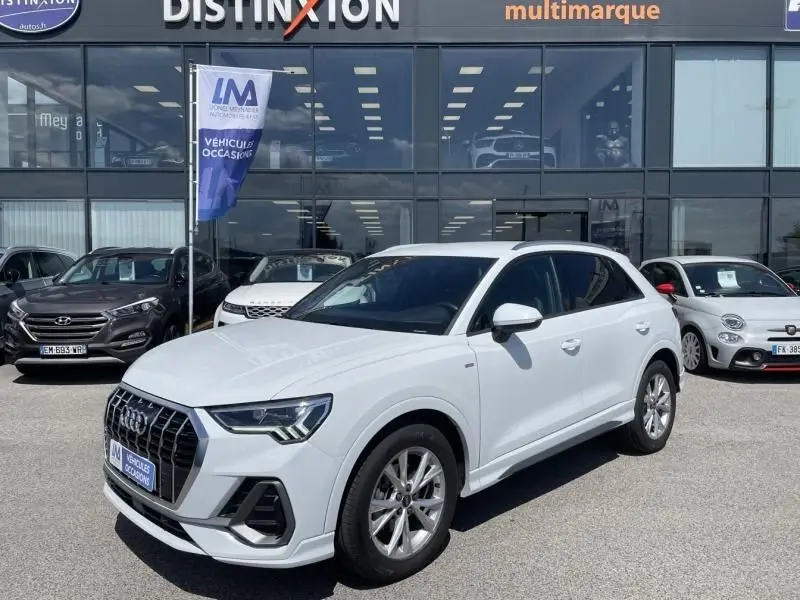 Audi Q3 blanc en 3/4 avant droit, version S-Line avec calandre distinctive et jantes alliage visibles.