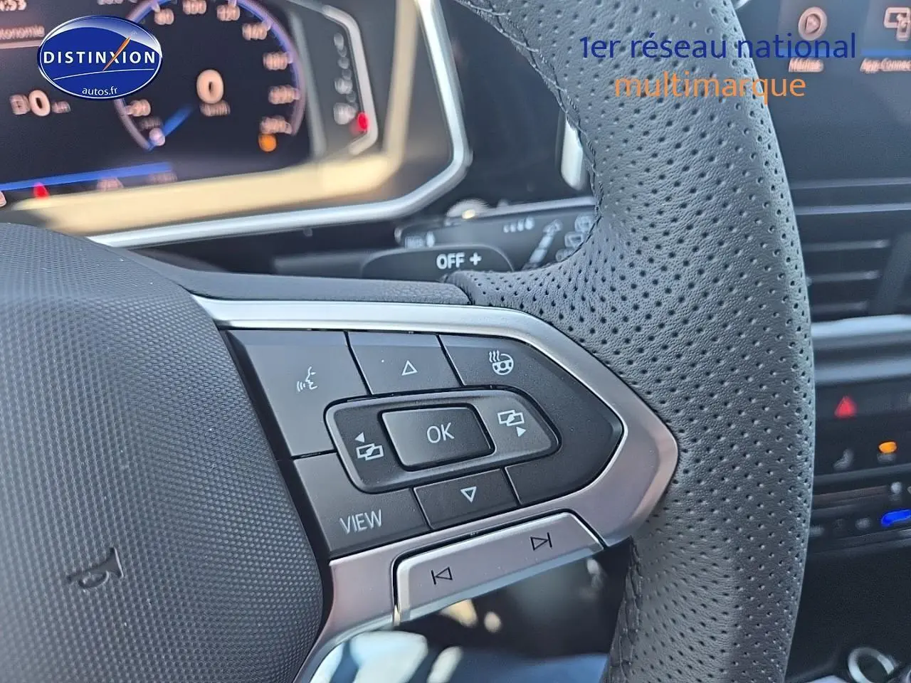 Gros plan sur le volant cuir perforé du Volkswagen T-Roc noir perle, avec commandes multifonctions et cockpit numérique en arrière-plan.