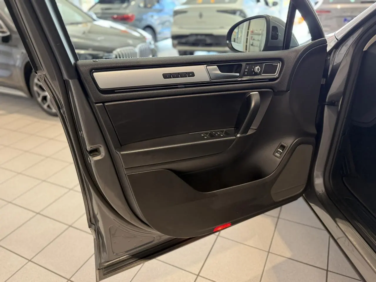 Porte avant gauche ouverte du Volkswagen Touareg gris foncé, montrant les commandes de vitres et le revêtement intérieur noir avec insert argenté.