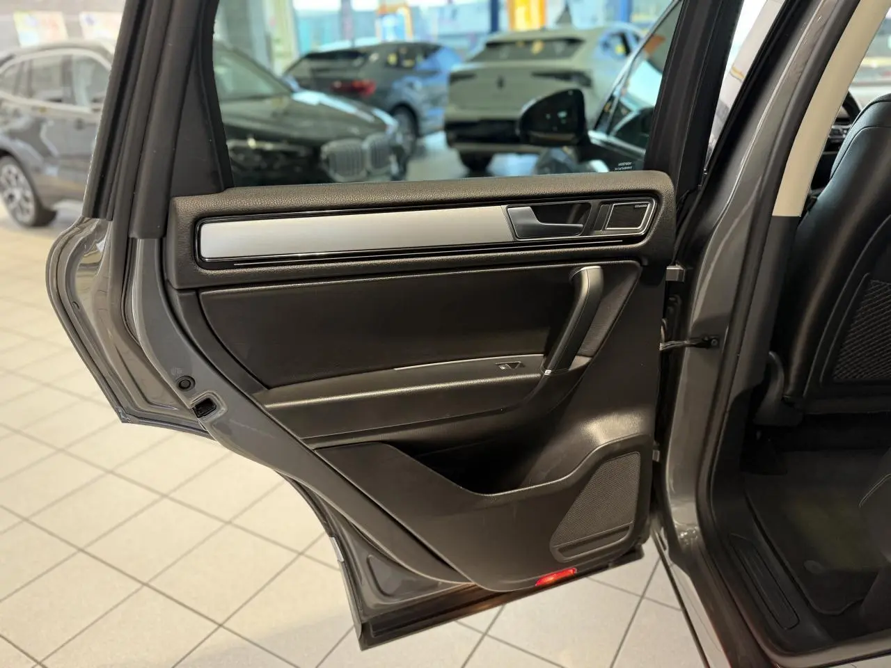 Porte arrière gauche ouverte du Volkswagen Touareg gris foncé, intérieur noir avec insert argenté et haut-parleur intégré.