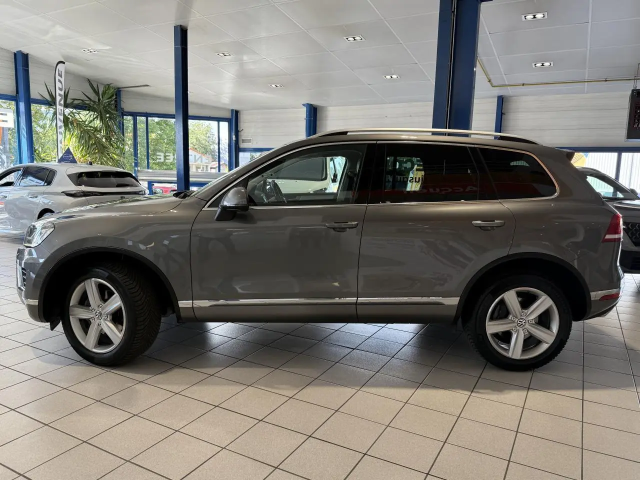 Volkswagen Touareg gris foncé vu de profil côté gauche, jantes alliage 19 pouces, intérieur showroom lumineux.
