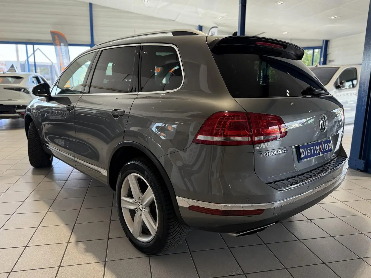 Vue 3/4 arrière droite d'un Volkswagen Touareg gris foncé en showroom, avec jantes alliage et vitres teintées.