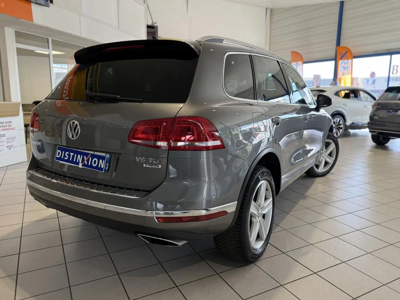 Volkswagen Touareg gris foncé en 3/4 arrière droit dans un showroom avec jantes alliage 19 pouces et vitres teintées.