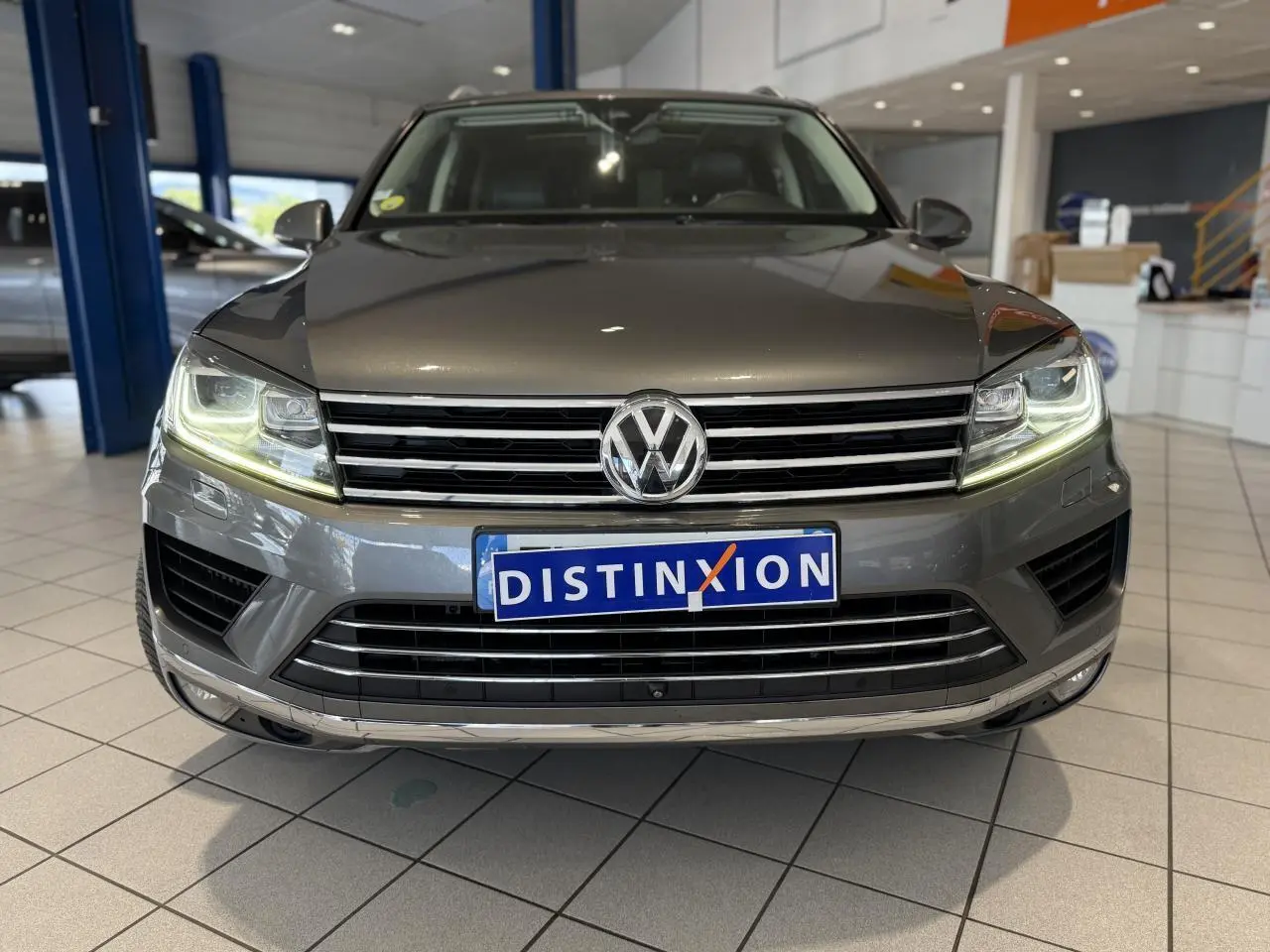 Vue de face du Volkswagen Touareg gris foncé avec phares allumés et calandre chromée en showroom.