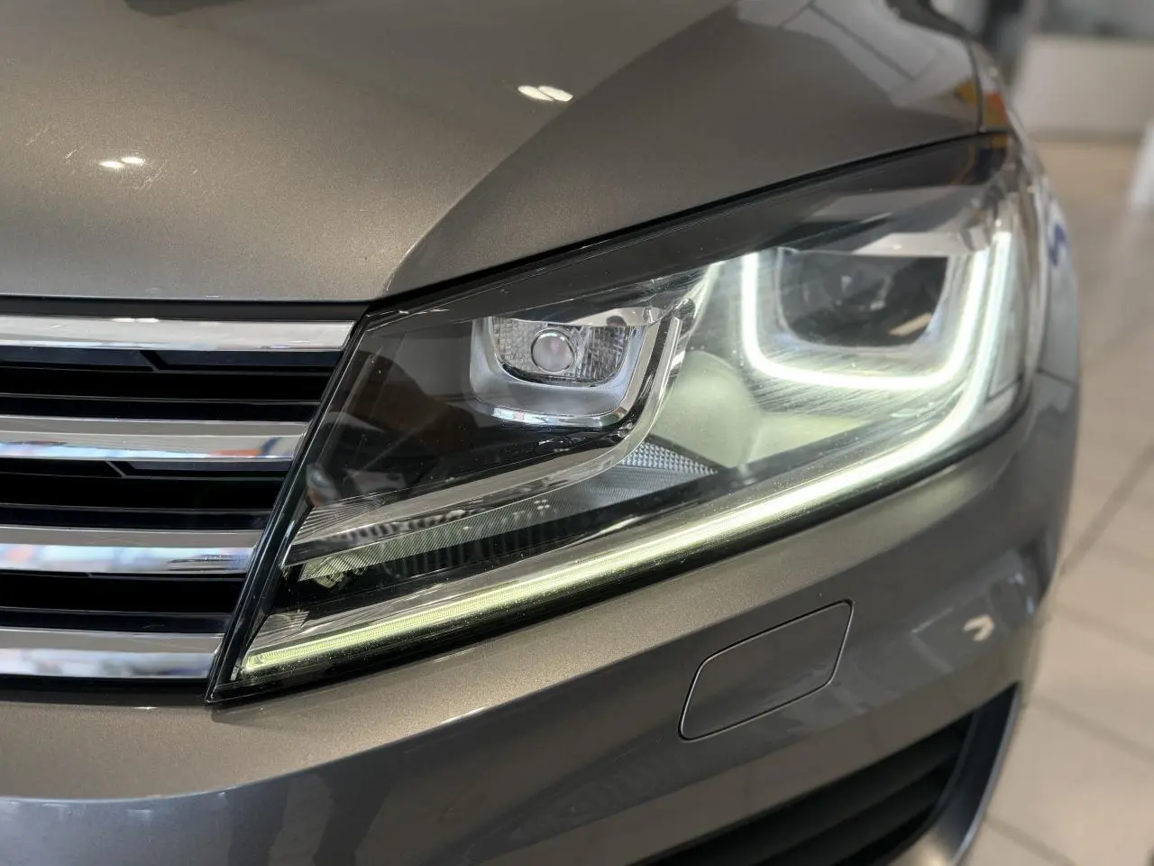 Gros plan sur le phare avant droit allumé d'un Volkswagen Touareg gris foncé, soulignant ses lignes modernes et LED distinctives.