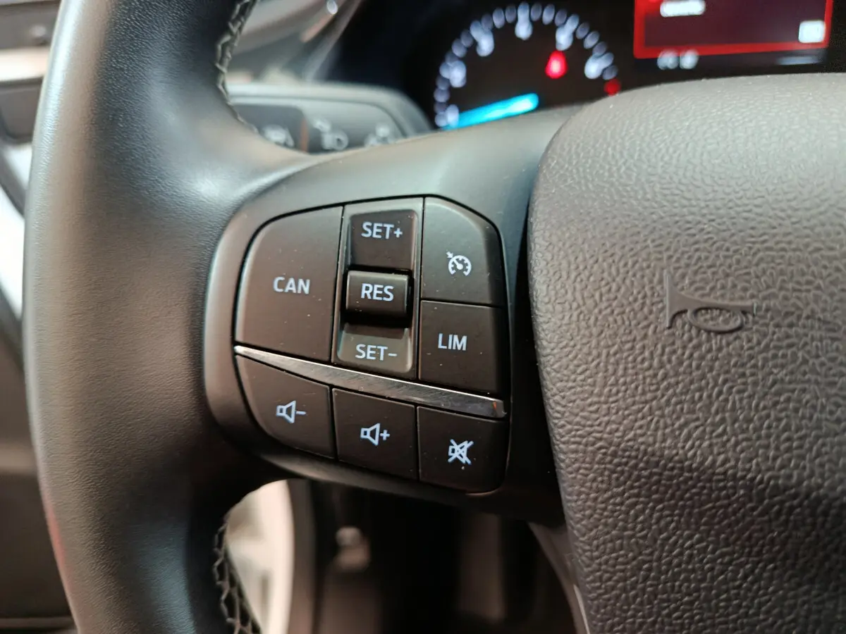 Gros plan sur les commandes au volant côté gauche du Ford Puma blanc 2022, avec affichage du tableau de bord en arrière-plan.