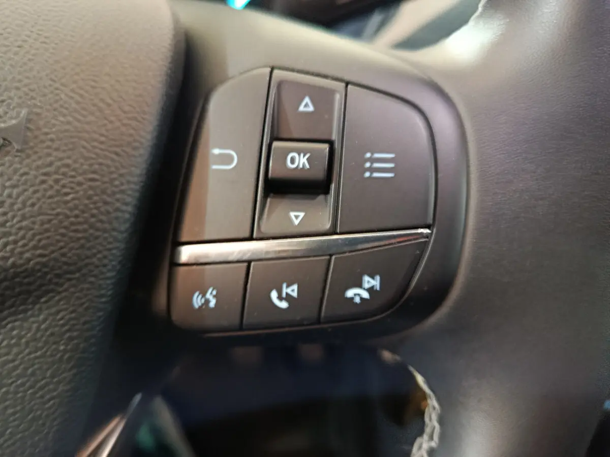 Gros plan sur les commandes multifonctions noires du volant en cuir d'une Ford Puma blanche, version Titanium 2022.