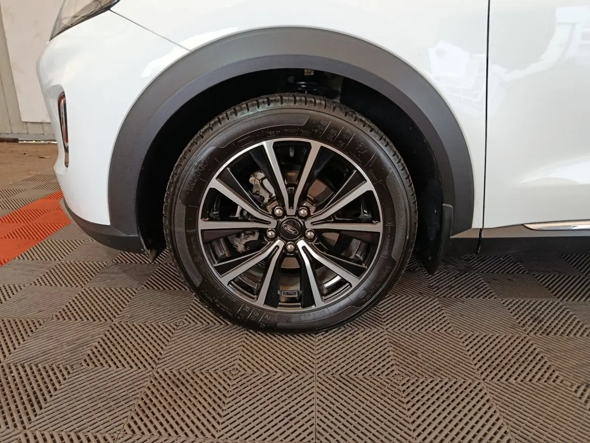 Gros plan sur la roue avant gauche noire et argentée du Ford Puma blanc, avec passage de roue en plastique noir.