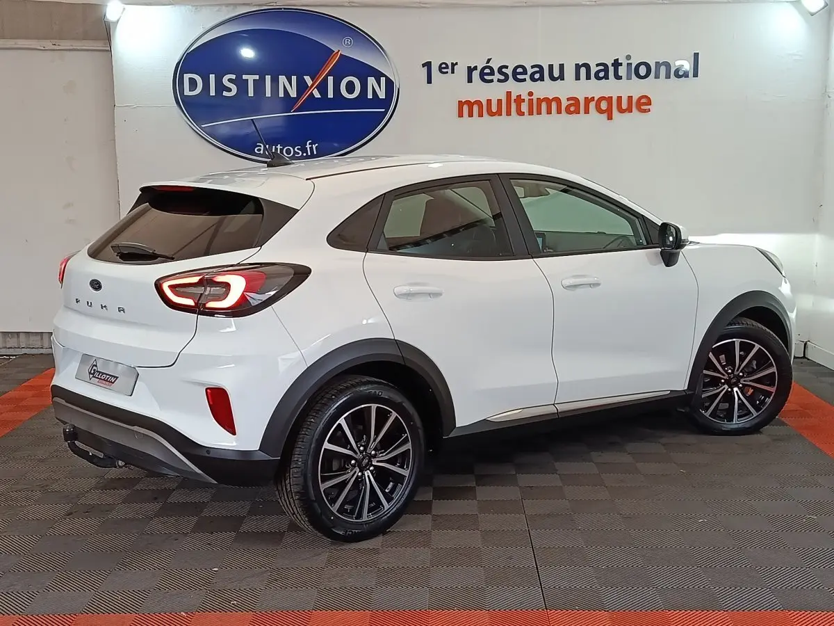 Vue 3/4 arrière droite d'un Ford Puma blanc 2022 avec feux arrière allumés et jantes noires en alliage.