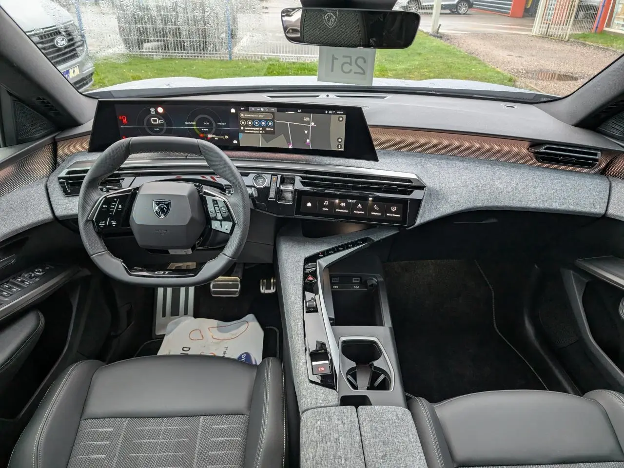 Vue intérieure avant du Peugeot 5008 gris 2025, tableau de bord moderne avec écran panoramique et volant compact noir.