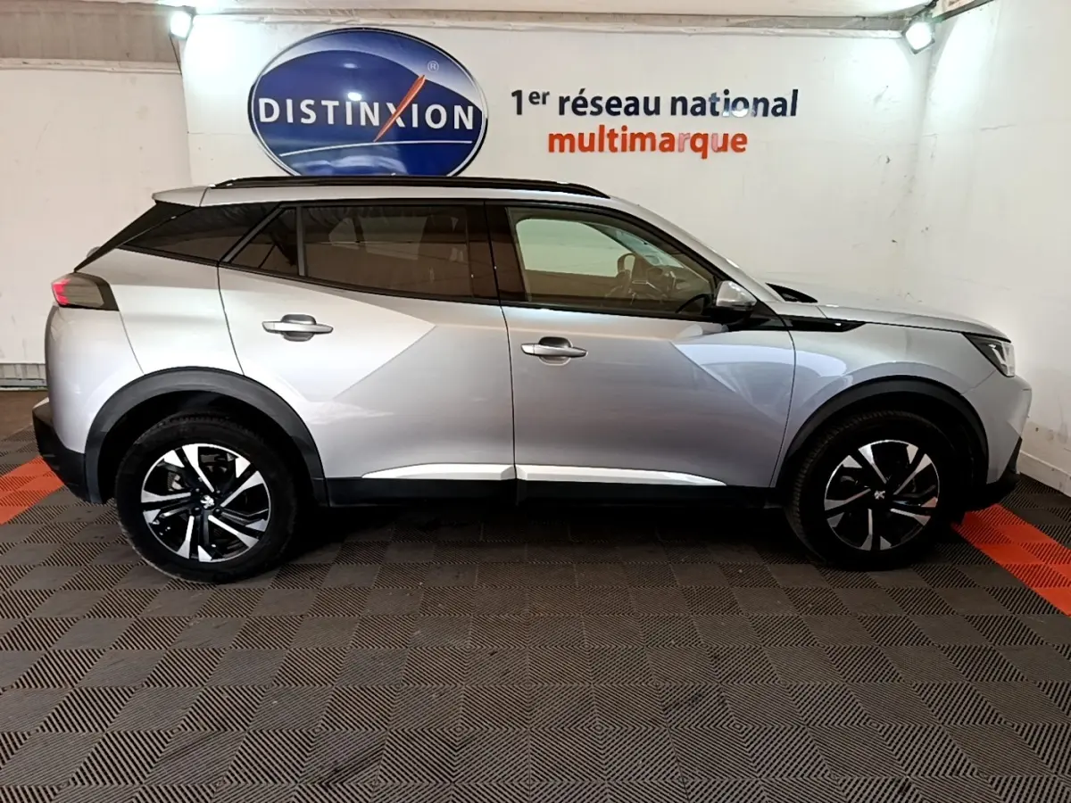 Profil droit d'un Peugeot 2008 gris clair 2021, avec jantes noires et toit noir contrasté en intérieur showroom.