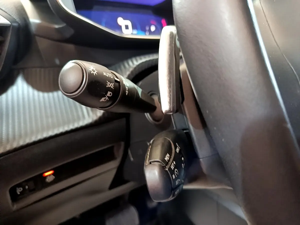 Gros plan sur les commandes au volant du Peugeot 2008 2021, montrant les leviers de clignotants et régulateur, intérieur noir.