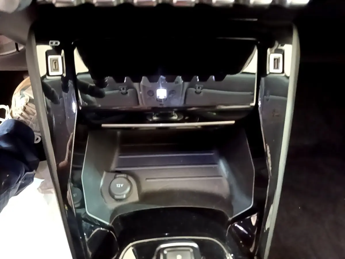 Vue plongeante sur la console centrale noire du Peugeot 2008 gris clair, avec prise 12V et rangement intégré.