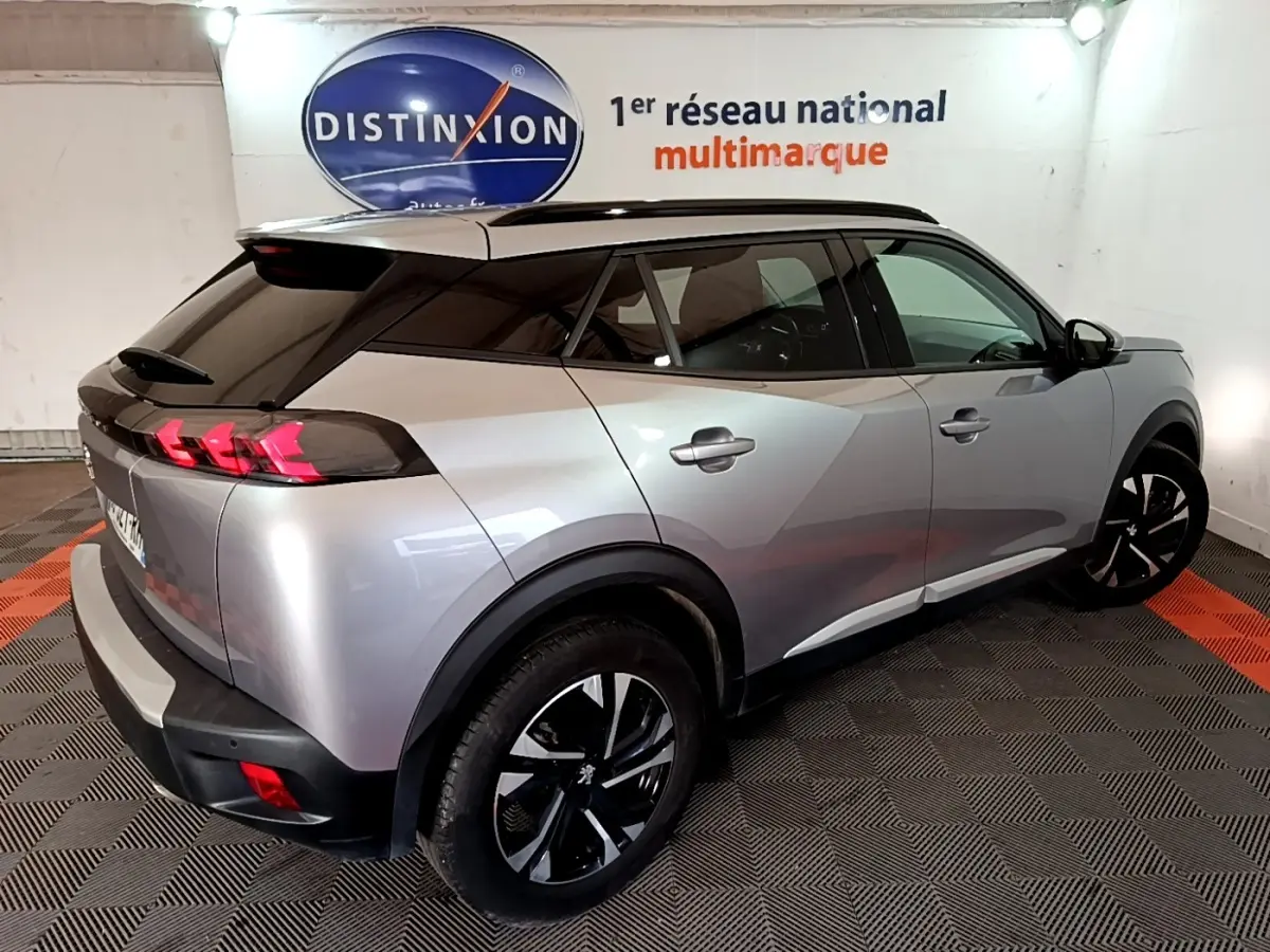 Peugeot 2008 gris clair vue 3/4 arrière droit, avec toit noir et feux arrière à effet griffes rouges.