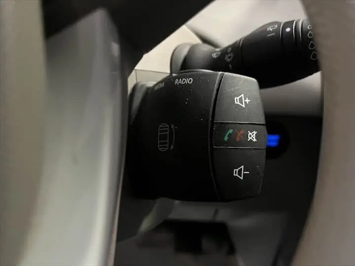 Gros plan sur la commande radio au volant d'une Renault ZOE blanc glacier, avec boutons de volume et appel visible.