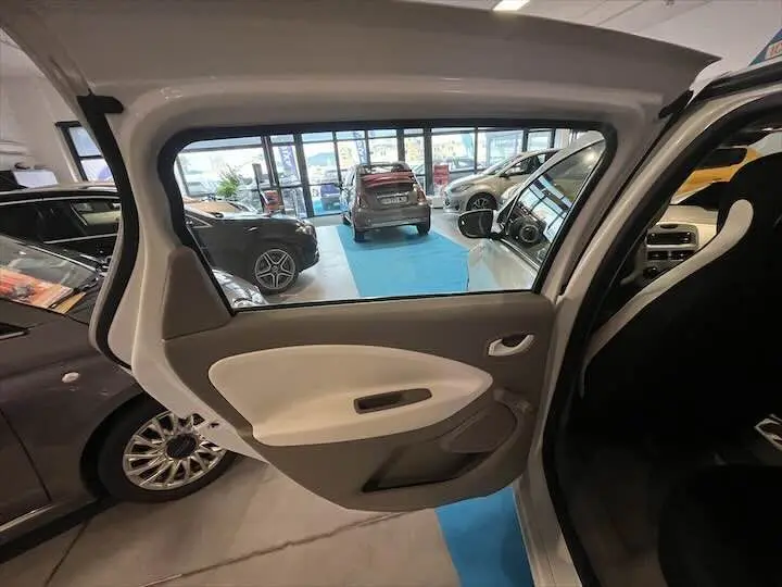 Vue intérieure de la porte arrière gauche ouverte d'une Renault ZOE blanc glacier dans un showroom lumineux.