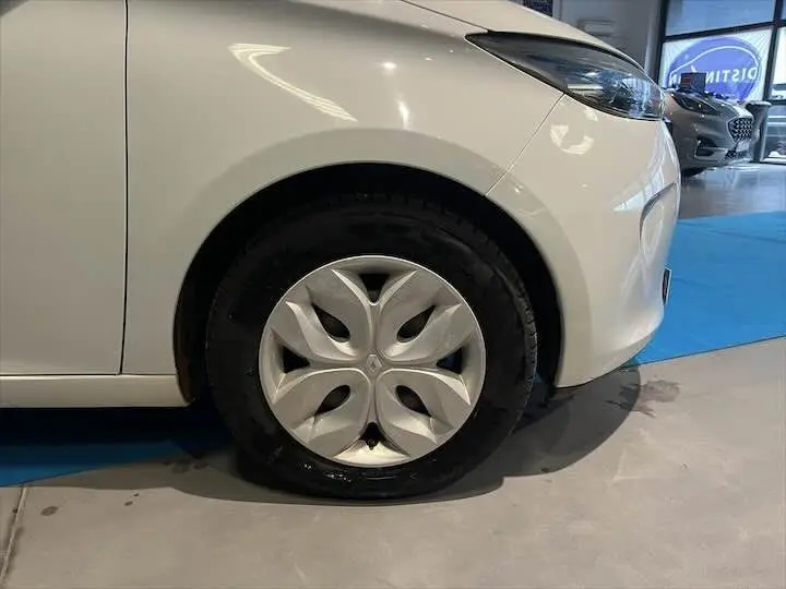 Gros plan sur la roue avant droite d'une Renault ZOE blanc glacier, mettant en valeur la jante au design distinctif.