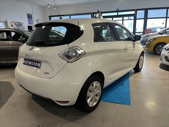 Vue 3/4 arrière droite d'une Renault ZOE blanche glacier en showroom avec toit noir et jantes pleines.