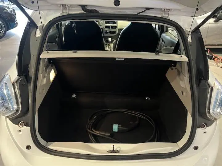 Coffre ouvert vu de l'arrière d'une Renault ZOE blanc glacier, avec câble de recharge électrique visible à l'intérieur.